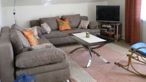 A living room with a sofa, a coffee table, a television, and a rocking chair.