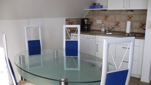 A modern kitchen with a glass dining table, blue chairs, white cabinets, and a coffee machine.