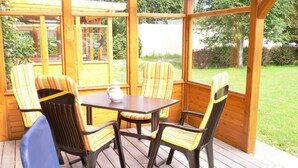 A wooden deck with a table and four striped chairs. - Holiday house with large garden, covered terrace, near the beach,  (Westerdeichstrich)