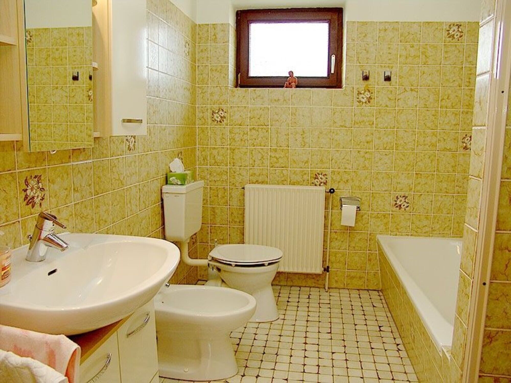 A bathroom with a sink, toilet, and bathtub, tiled with a yellow pattern.