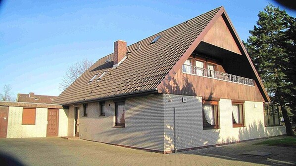A two-story house with a sloped roof, a balcony on the upper floor, and a brick exterior.