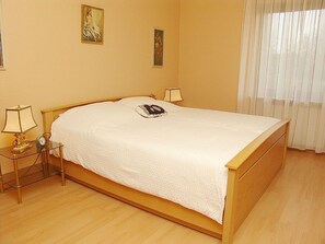 A neatly made bed in a room with a wooden floor, two bedside tables with lamps, and two framed pictures on the wall.
