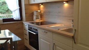 A compact kitchen with white cabinets, a built-in oven, a microwave, and a sink. - Holiday house with large garden, covered terrace, near the beach,  (Westerdeichstrich)