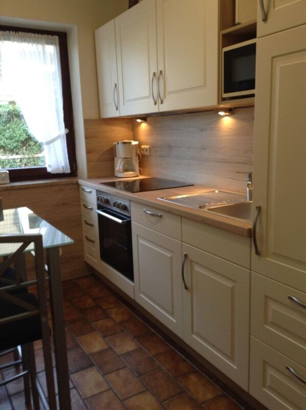 A compact kitchen with white cabinets, a built-in oven, a microwave, and a sink. - Holiday house with large garden, covered terrace, near the beach, (Westerdeichstrich)