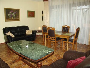 A living room with a black leather sofa, a wooden dining table with chairs, a marble coffee table, and a painting on the wall. - Holiday house with large garden, covered terrace, near the beach, (Westerdeichstrich)
