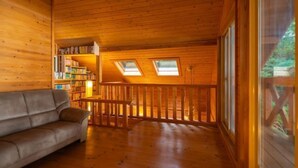 L’intérieur d’un chalet en bois, avec un canapé, des étagères et un balcon doté de lucarnes.