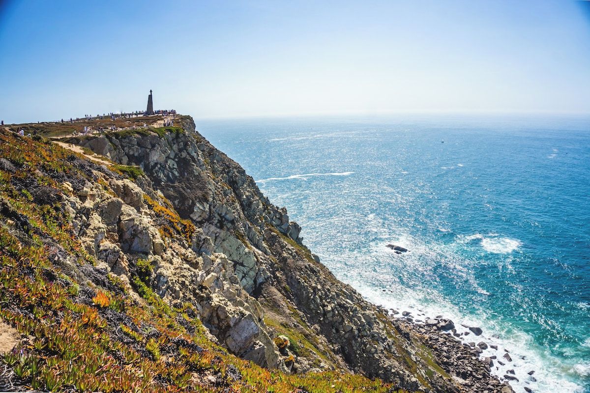 A coastal landscape with a rocky cliff, a lighthouse, and the ocean.