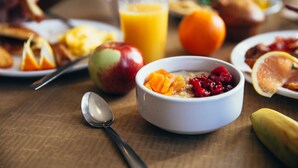 A breakfast setting with a bowl of cereal, a glass of orange juice, and various fruits on a wooden table. - Hotel Montriond (Val d'Illiez)