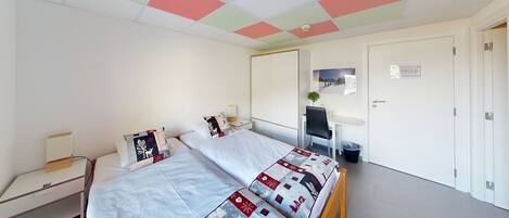 A hotel room with a bed, bedside tables, a desk, and a chair.