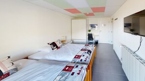 A room with two beds, a desk, a chair, a radiator, and a TV. - Hotel Montriond (Val d'Illiez)