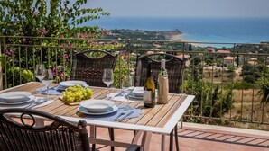 A table set for two with a view of the sea, a bottle of wine, and a bowl of grapes. - Countrystyle Villa Bonora (Skala Kefalonias)