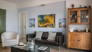 A living room with a dark leather sofa, a glass coffee table, and a wooden cabinet with glass doors. - Countrystyle Villa Bonora (Skala Kefalonias)