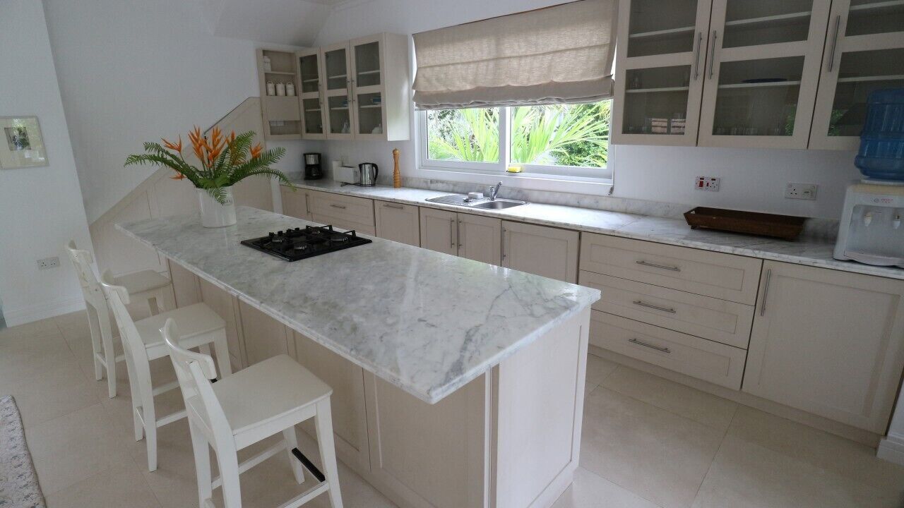 A kitchen with a marble countertop, white cabinets, and a window with a view of greenery.