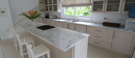 A kitchen with a marble countertop, white cabinets, and a window with a view of greenery.