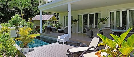 A poolside area with lounge chairs, a covered seating area, and a view of the pool.