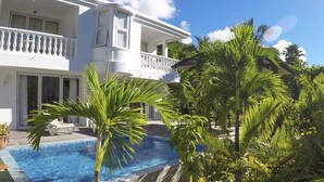Un bâtiment blanc doté d’un balcon, d’une piscine et de plantes tropicales.