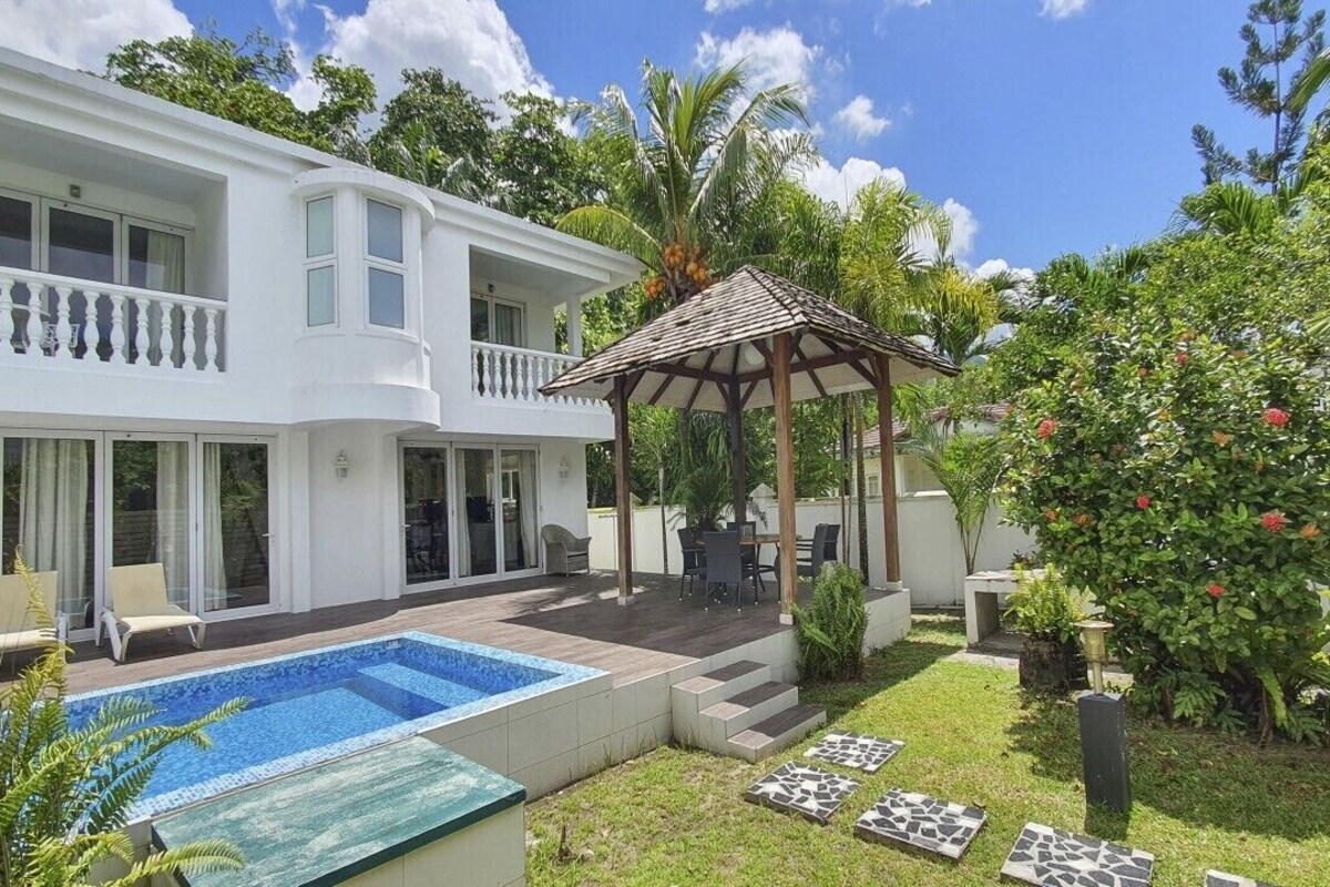 A two-story house with a swimming pool, a covered patio, and a garden with tropical plants.
