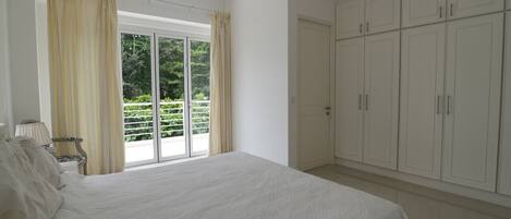Una camera da letto con un letto grande, una porta scorrevole in vetro che dà su un balcone e armadi bianchi.