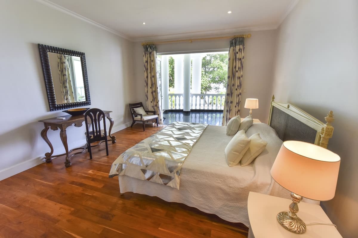 A bedroom with a bed, a desk, a chair, a lamp, and a balcony with curtains.