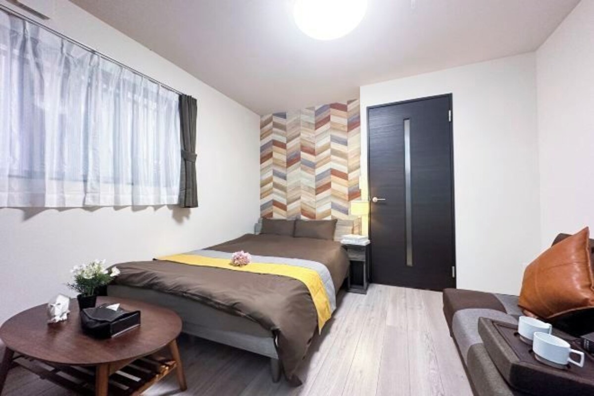 Een kleine hotelkamer met een enkel bed, een tafeltje, een bank en een deur.