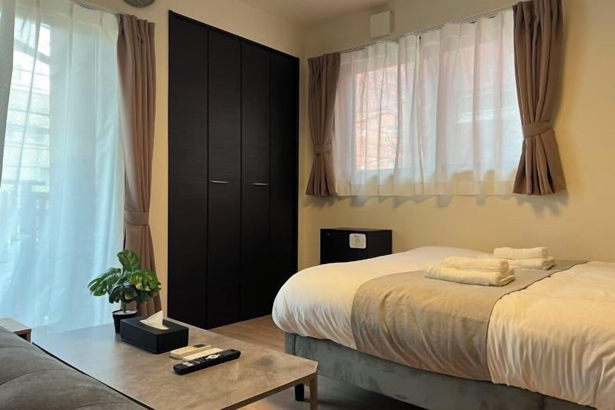 Une chambre à coucher avec un lit, un bureau avec une télécommande, une plante en pot et une armoire.
