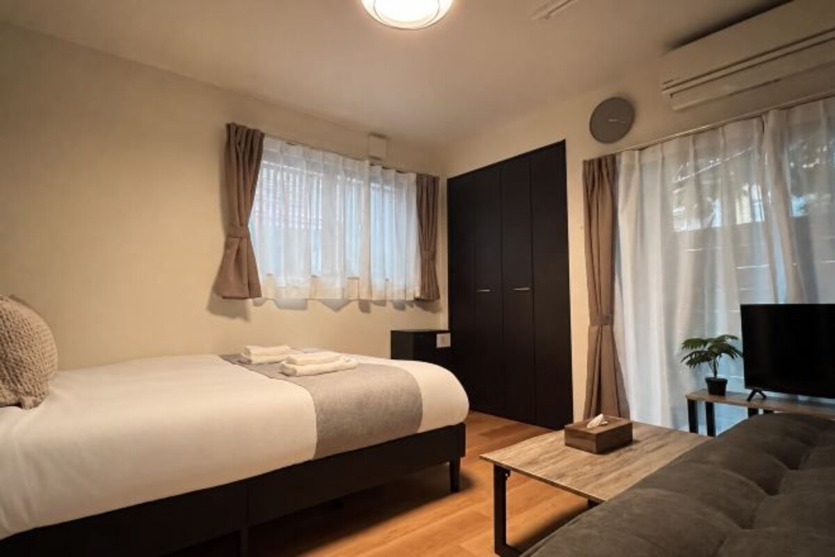 A bedroom with a bed, a sofa, a TV, and a window with curtains.