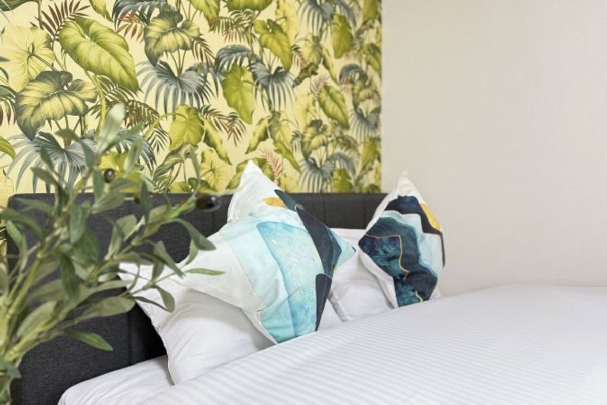 A hotel room with a bed, pillows, and a wall with a tropical plant pattern.