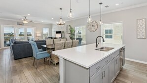 A modern kitchen with a central island, a dining area with a sofa and chairs, and a large window with blinds. - Monthly Rates Available | Footloose Lost Key Resort | Pet Friendly | Free Golf | Beach Club | Pools (Pensacola)