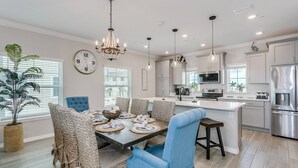 A modern kitchen with a central island, stainless steel appliances, and a dining area with wicker chairs and a blue upholstered chair. - Monthly Rates Available | Footloose Lost Key Resort | Pet Friendly | Free Golf | Beach Club | Pools (Pensacola)