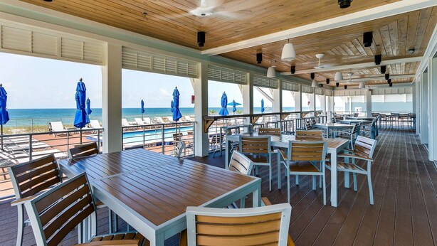 A covered outdoor dining area with wooden tables and chairs, overlooking a pool and beach. - Monthly Rates Available | Footloose Lost Key Resort | Pet Friendly | Free Golf | Beach Club | Pools (Pensacola)