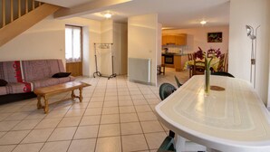 Een ruime woonkamer met een bank, salontafel en een eettafel met stoelen. Een trap is zichtbaar op de achtergrond, leidend naar een andere kamer.