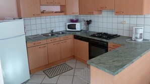 Een kleine keuken met houten kastjes, een magnetron, een gasfornuis en een koffiezetapparaat.