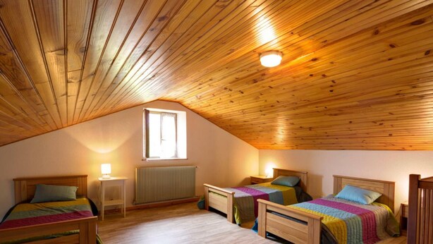 Un dormitorio abrigado en el ático, con listones de madera en el techo, dos camas individuales, una ventana y un radiador.