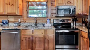 A kitchen with wooden cabinets, a stainless steel refrigerator, a microwave, an oven, and a sink with a window above it. - Moonlight Obsession, a Secluded Dog-Friendly Cabin located just minutes from downtown Gatlinburg (Gatlinburg)