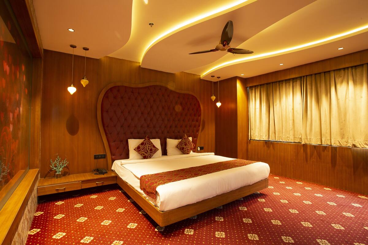 A hotel room with a large bed, a ceiling fan, and a window with curtains.