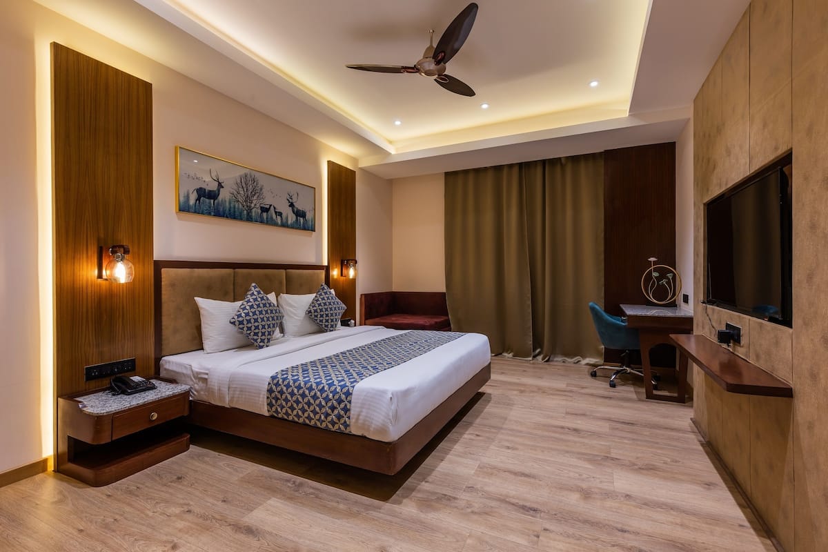 A modern hotel room with a large bed, a desk, a chair, a ceiling fan, and a TV.