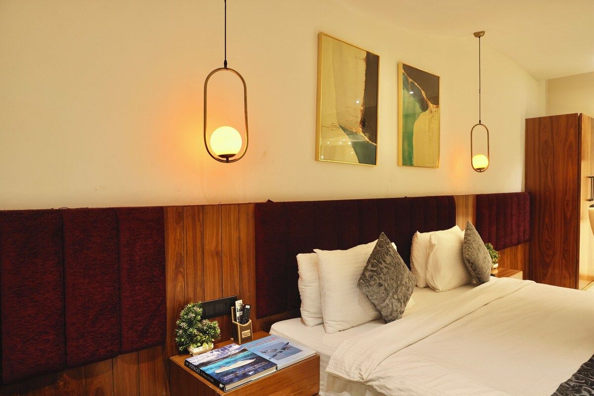 A hotel room with a wooden headboard, a bed with white linens, two wall-mounted light fixtures, and a framed abstract painting.
