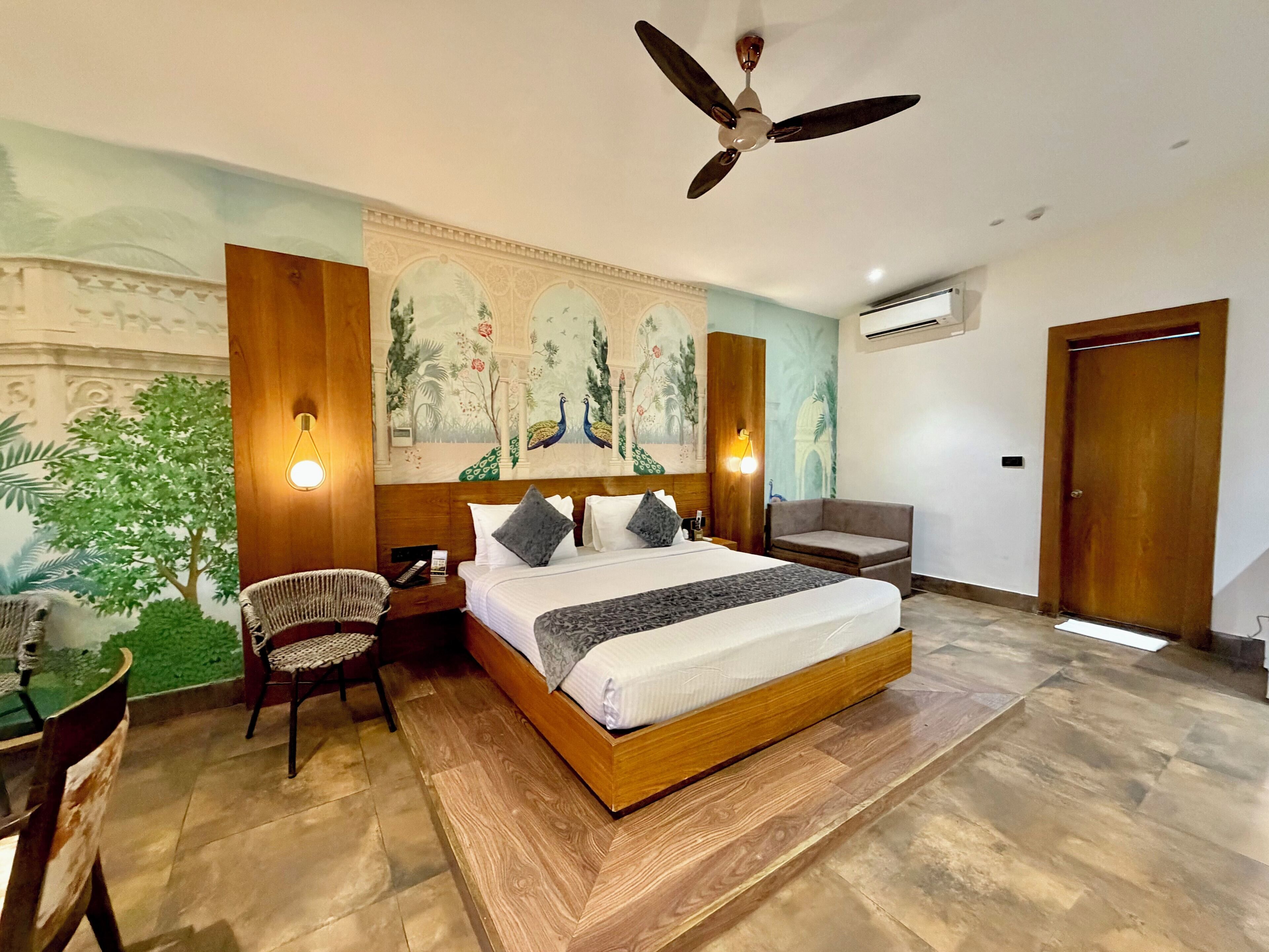 A bedroom with a bed, a ceiling fan, a nightstand, a chair, a wall mural, and an air conditioning unit.