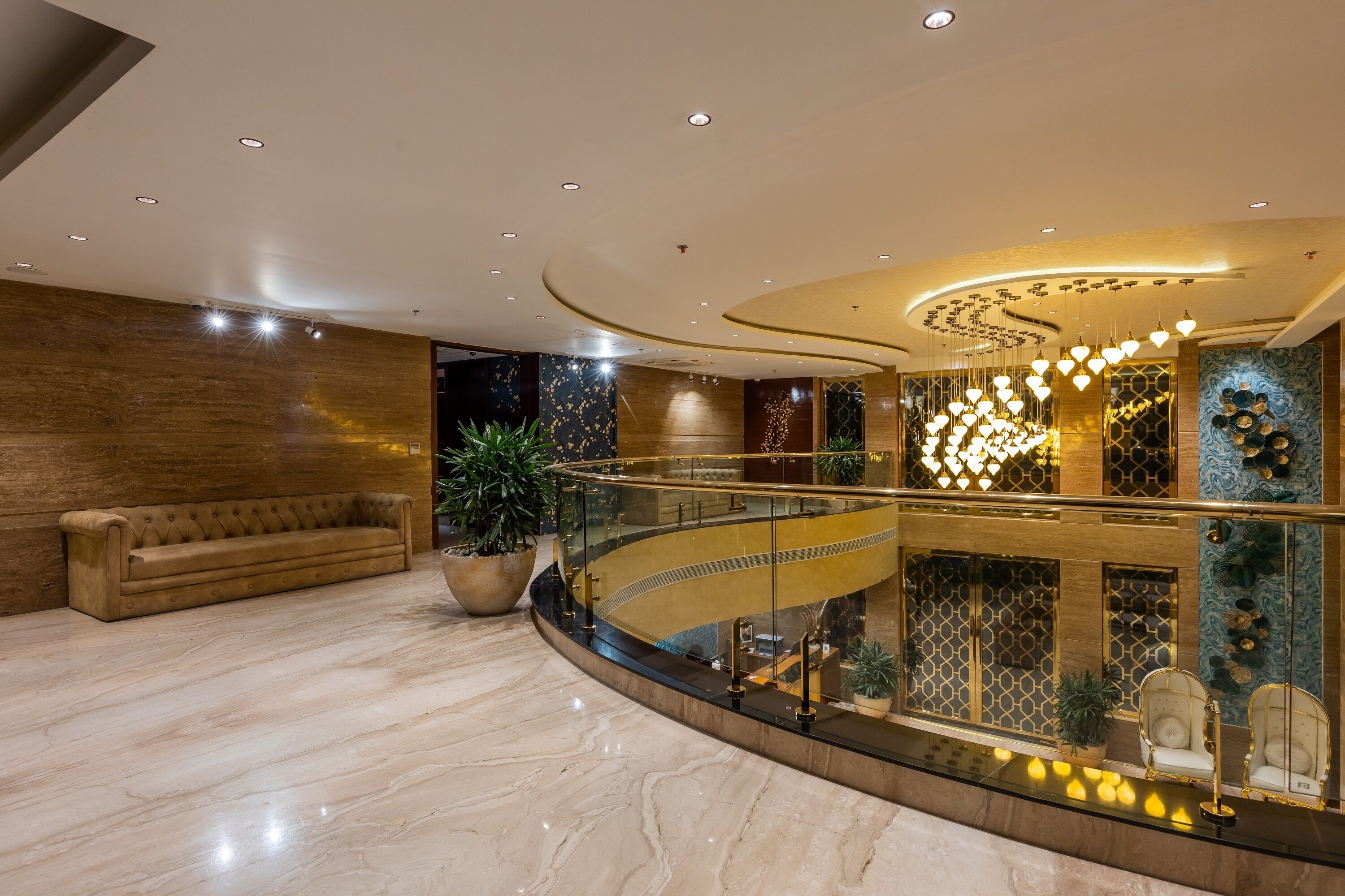 Un hall d’entrée spacieux avec un sol en marbre, un canapé en cuir, une balustrade en verre et un lustre décoratif.