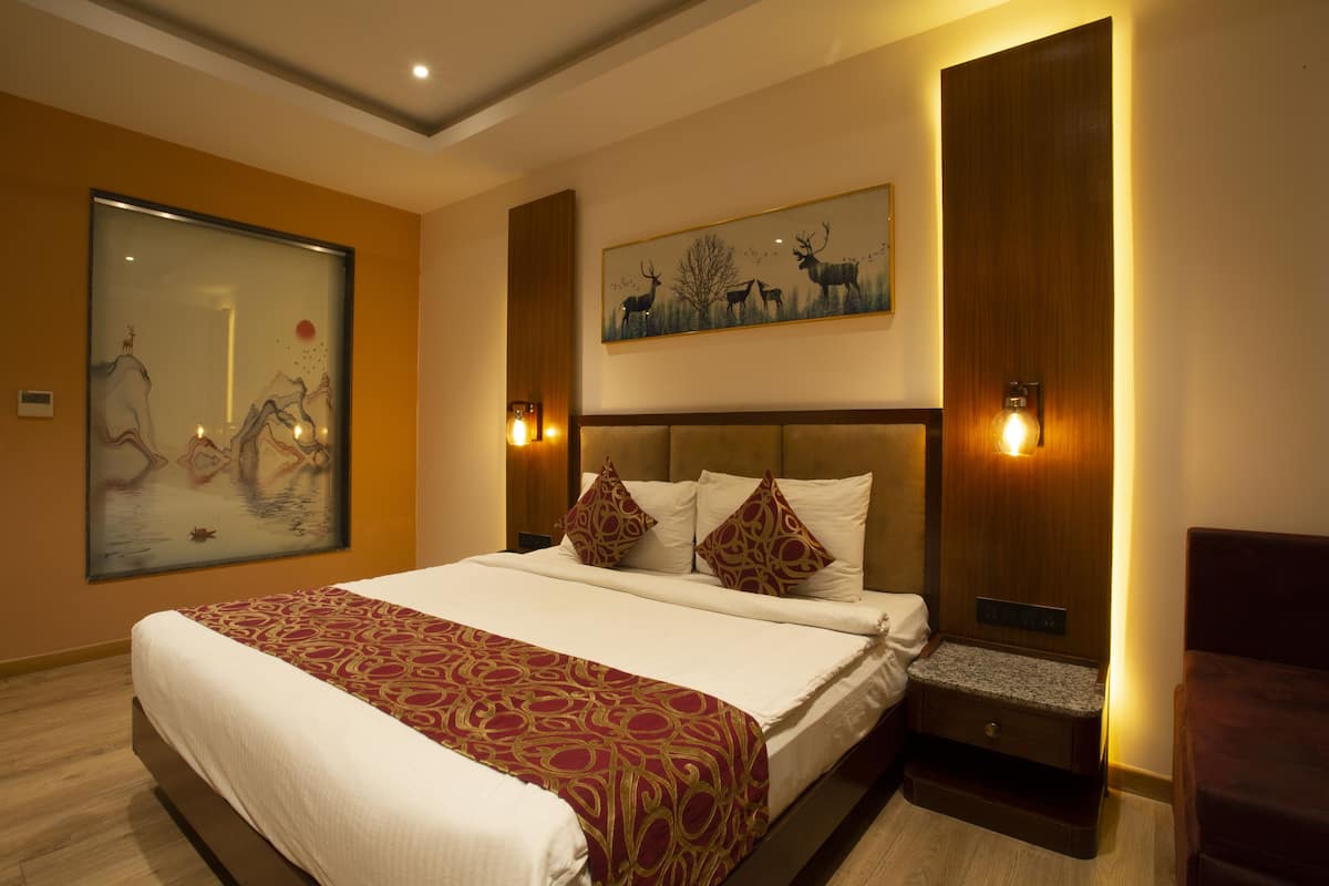 A hotel room with a large bed, a nightstand, a wooden wardrobe, and a painting on the wall.