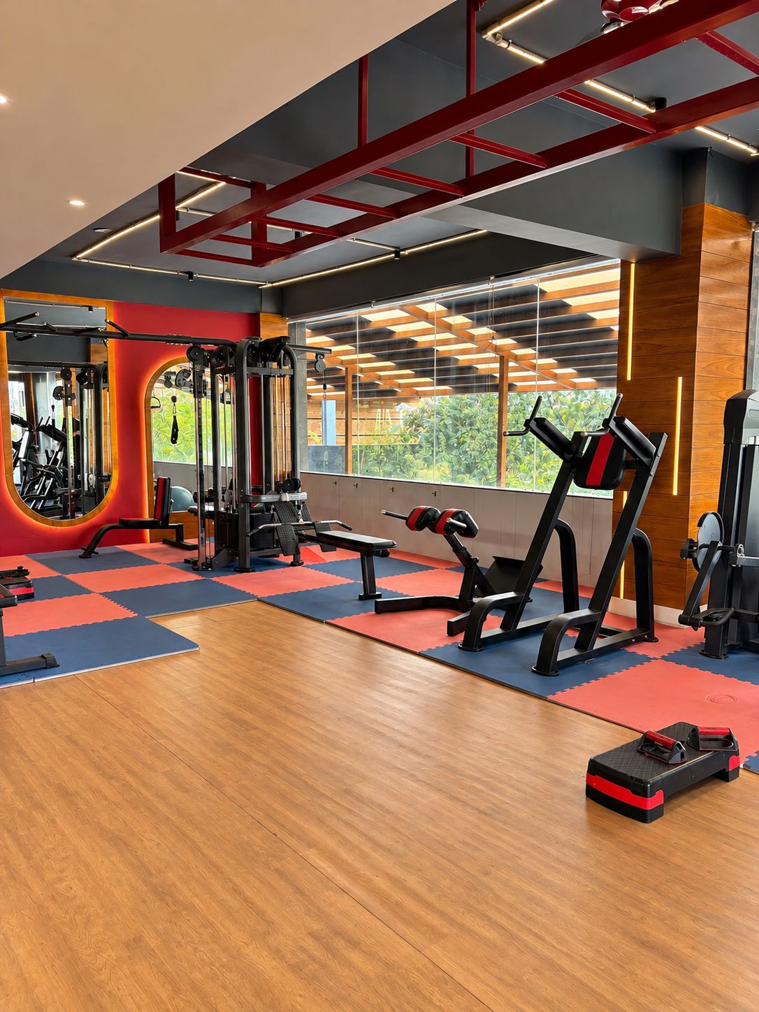 Ein Fitnessraum mit Trainingsgeräten, Holzböden und großen Fenstern.