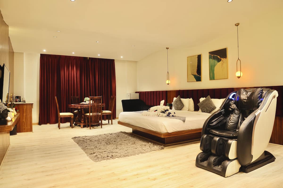 A modern hotel room with a bed, massage chair, dining area, and artwork on the walls.