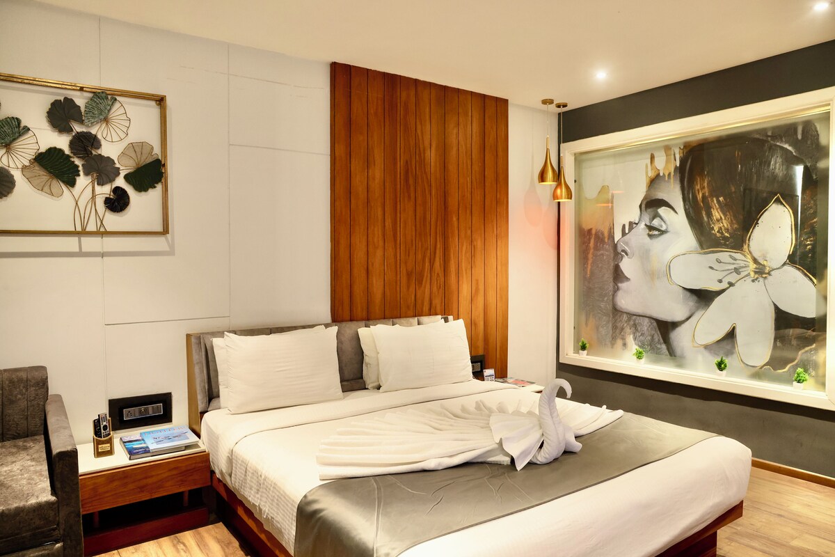 A modern hotel room with a bed, a nightstand, a lamp, and a large floral painting on the wall.