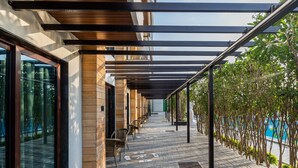 A covered outdoor area with a row of chairs, a tiled floor, and a pool in the background. - Skyline Resort & Convention Centre (Indore)