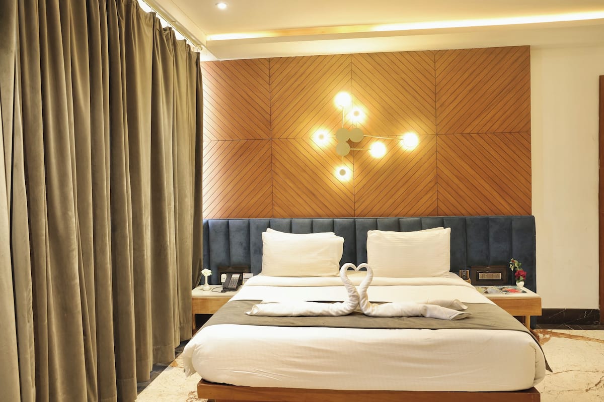 A hotel room with a large bed, a wooden headboard, a nightstand, and a wall-mounted light fixture.