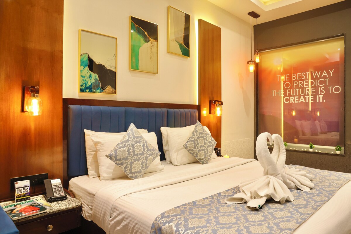 A hotel room with a bed, pillows, a bedside table with a phone, a magazine, and a window with a motivational quote.