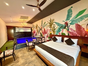 A hotel room with a bed, a desk, a chair, a small pool, and a large mural of tropical plants. - Skyline Resort & Convention Centre (Indore)
