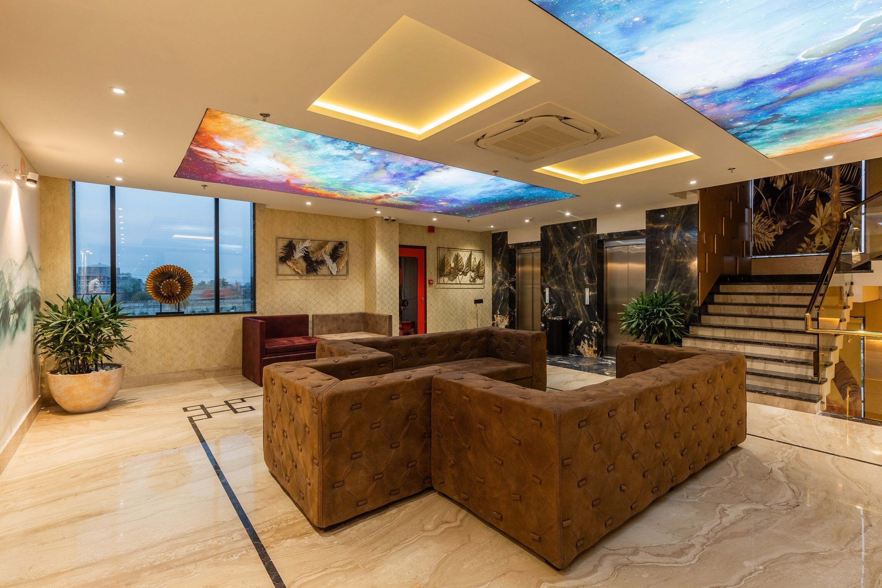 A modern lobby with a large seating area, a staircase, and a ceiling with a galaxy mural.