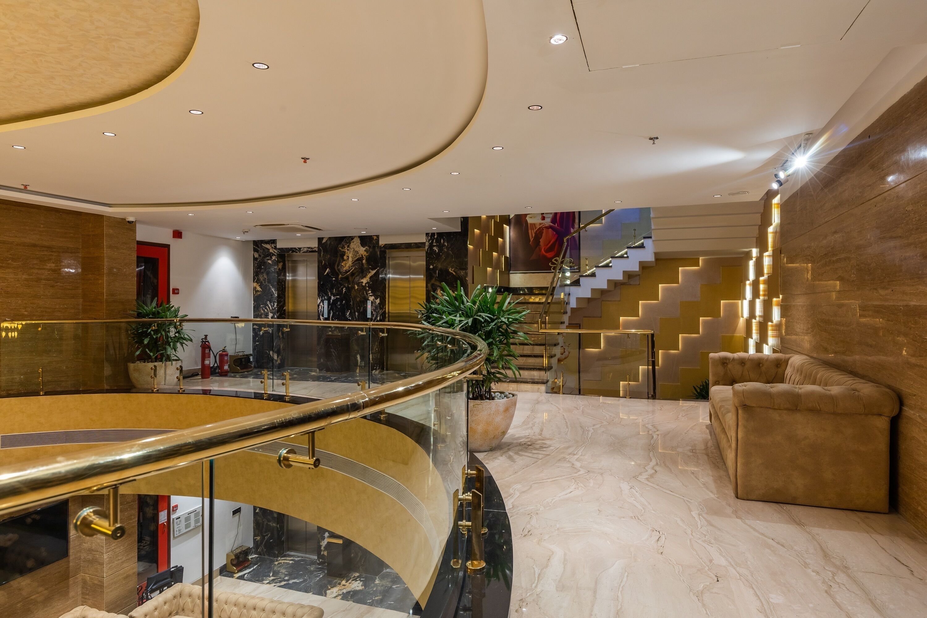 A modern lobby with a curved staircase, marble flooring, and a plush sofa.
