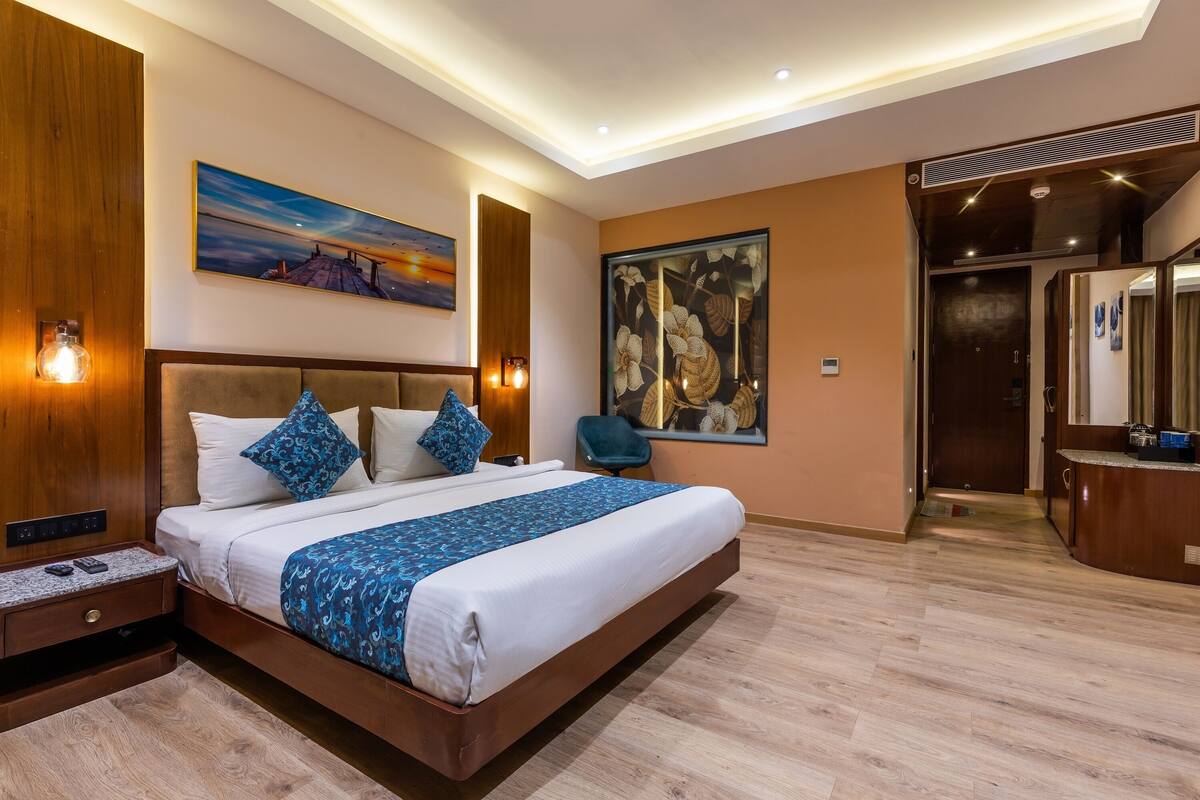 A modern hotel room with a large bed, a nightstand, a desk, and a bathroom visible through an open door.